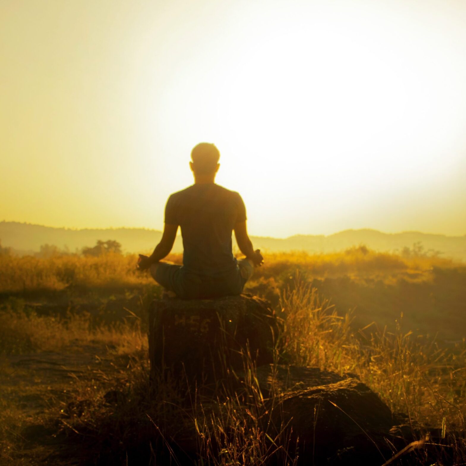 A backlit image of a man meditating with a setting sun.